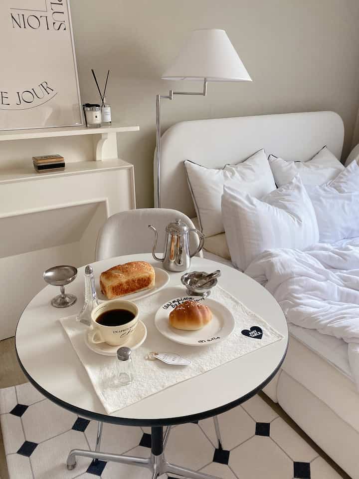 白とベージュのトーンの寝室、丸テーブルにコーヒーとパンが並ぶ心地よいおうちカフェの雰囲気のあるインテリア