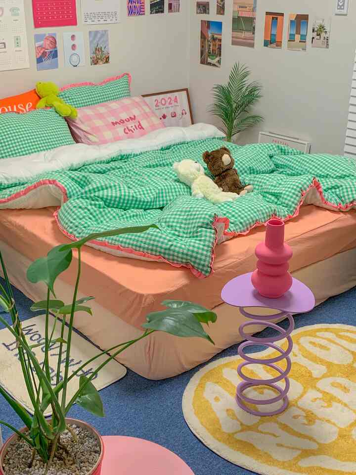 A cozy studio bedroom with pink and green tones featuring playful bedding and decorative plants
