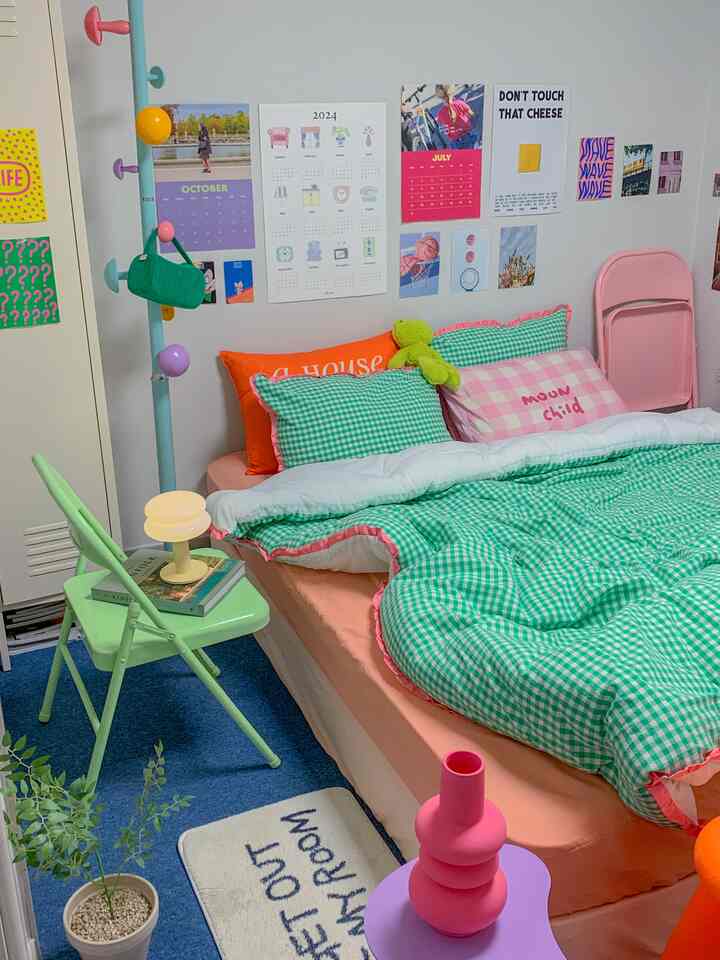 パステル調の色合いと白い壁のワンルーム寝室、緑のチェック柄寝具と折りたたみ椅子が配置された雰囲気のある空間