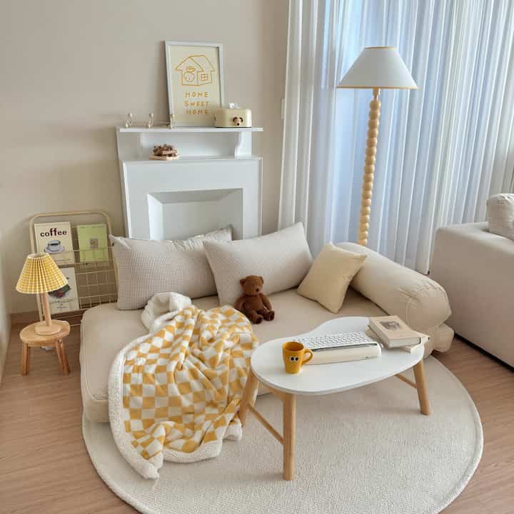 温かみのあるベージュと黄色の調和が取れたリビング、チェック柄のブランケットがかかった大きな座布団セットと木製小物が配置された雰囲気のあるインテリア