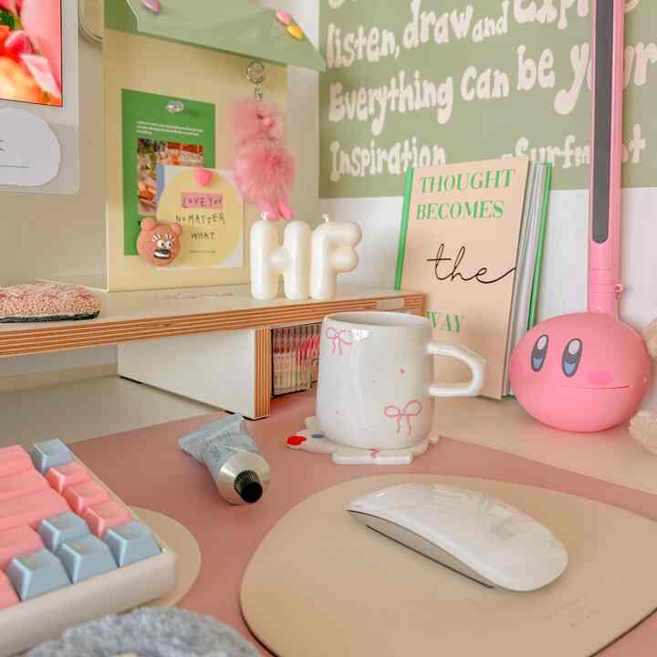 A cozy home office desk featuring pink and white tones, with books, a mouse, and a desk lamp arranged neatly