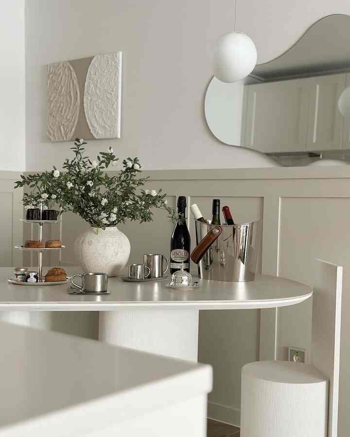 ニュートラルトーンのキッチンスペース、シルバーウェアとワインクーラーを置いたダイニングテーブルに花瓶と多段トレイが配置されたモダンなインテリア