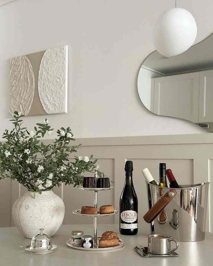 White and beige toned dining room featuring a silver tiered cake stand and wine bottles, creating a stylish home cafe atmosphere