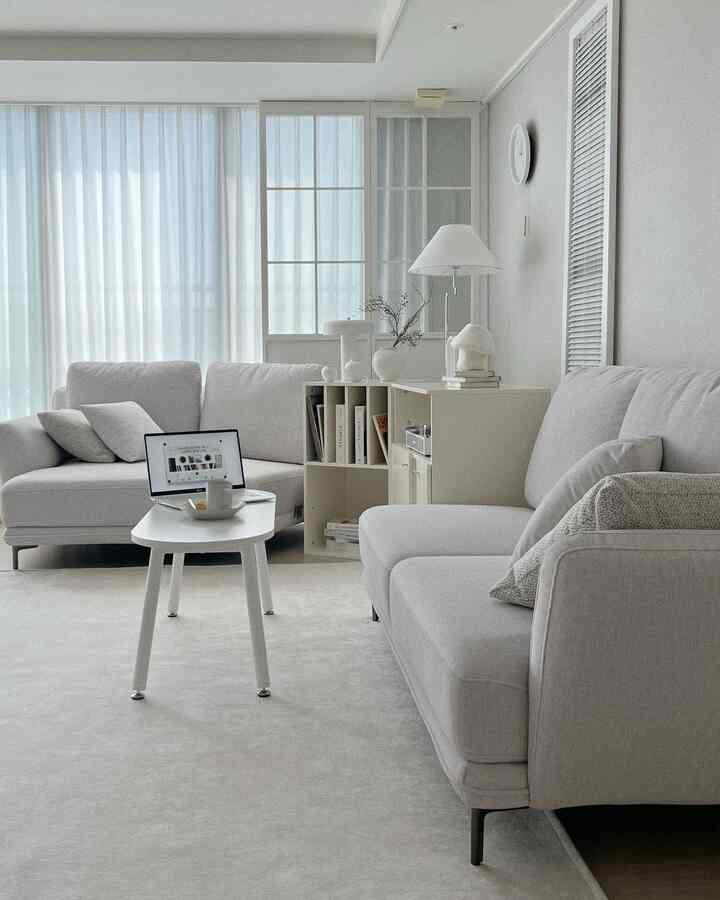White-toned living room with chiffon curtains and sofas, featuring a simple modern space with a laptop table