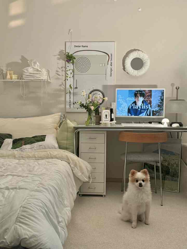 白とベージュの色調のリビング兼寝室、カーペットの上に犬が座り、ミッドセンチュリーモダン風のすっきりとしたデスクが配置された落ち着いた空間