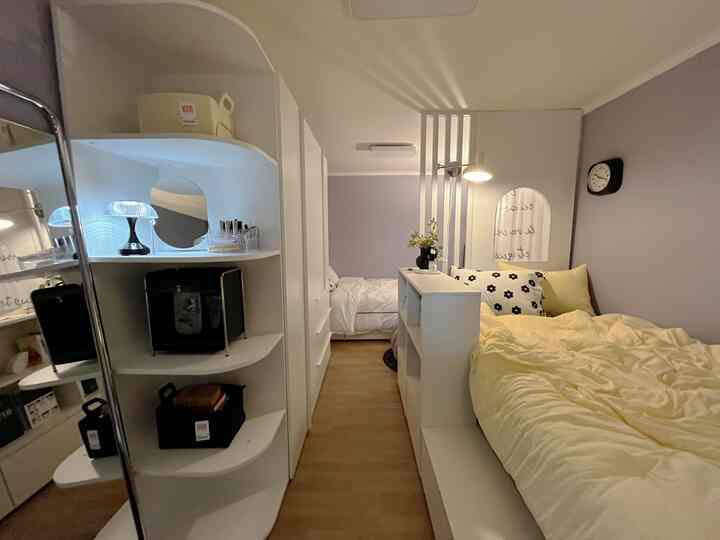 ホワイトとベージュの色調のワンルーム寝室、収納棚と2つのベッドが配置された雰囲気のあるインテリア