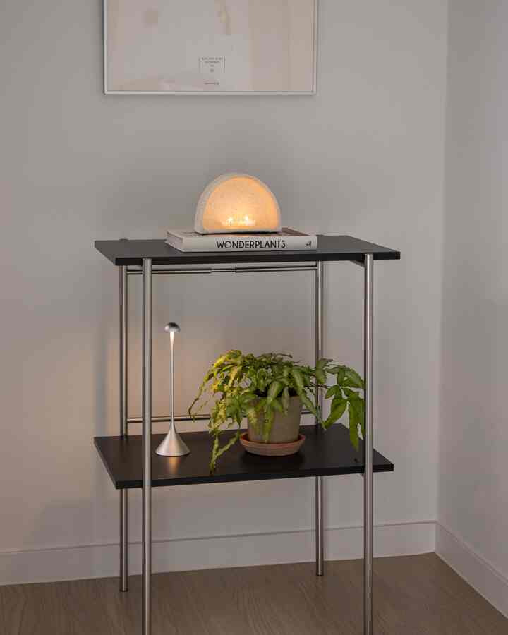 Natural-toned small nightstand featuring plant, wireless lamp, and candle warmer in a modern, clean interior space