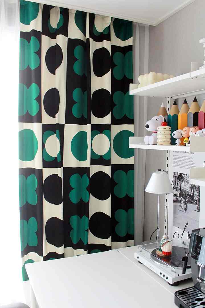 Bright, cozy space with white desk and shelves, dominated by black and green patterned curtain