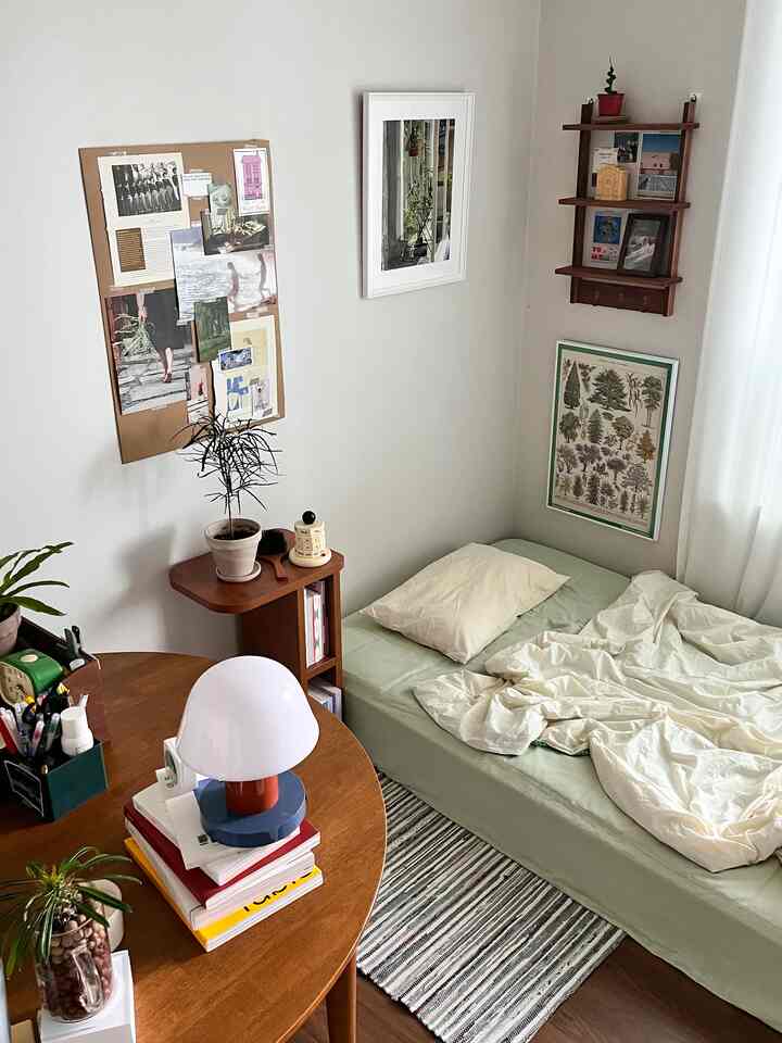 白い壁と木目調の家具が調和した一人暮らしの寝室、シンプルにまとめられたベッド空間と大きな額縁、ラグが特徴のインテリア