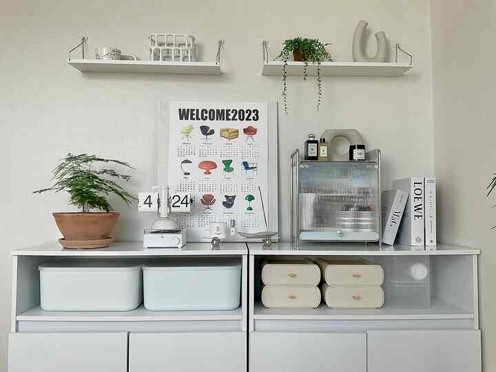 白を基調としたミニマルな収納家具が配置され、ポスターと植物のオブジェが印象的な雰囲気のあるインテリア