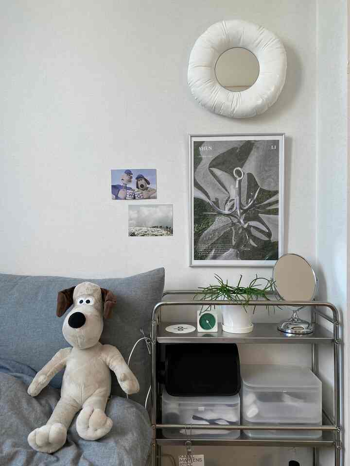 ホワイトの壁面に、グレーのソファとミッドセンチュリーモダン風のステンレス移動式トロリーが配置されたキッチン。グロミットのぬいぐるみとクッションミラーがあり、雰囲気のあるインテリア