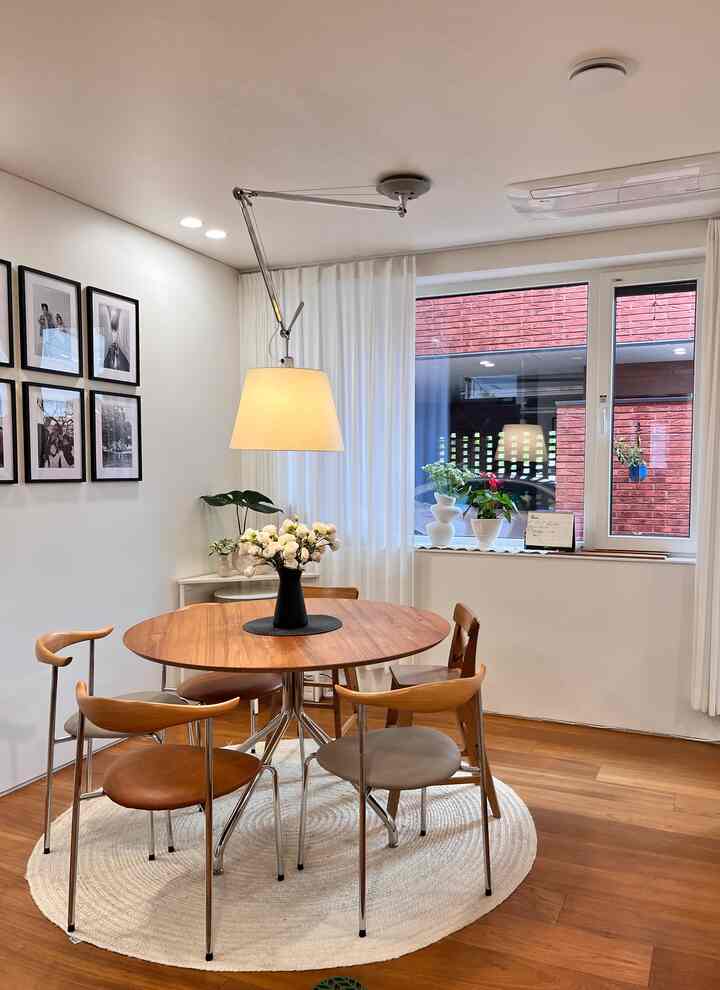 白い壁とナチュラルな木製ラウンドダイニングテーブル、5脚の木製チェアとペンダントライトが配置された印象的なダイニング空間