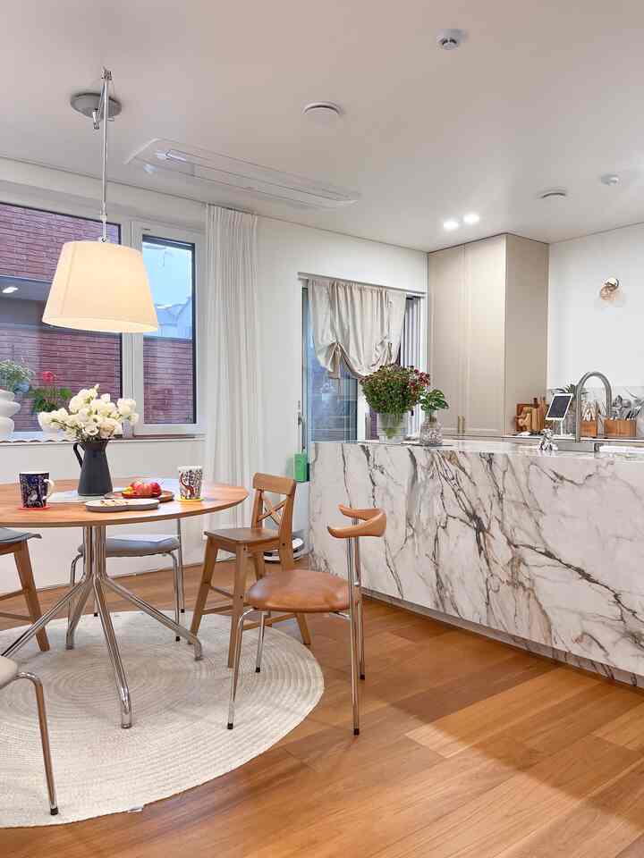 ホワイトの壁と天井を背景に、ナチュラルカラーのダイニングルーム。木製の丸テーブルと椅子、ペンダントライトが配置された雰囲気のあるインテリア