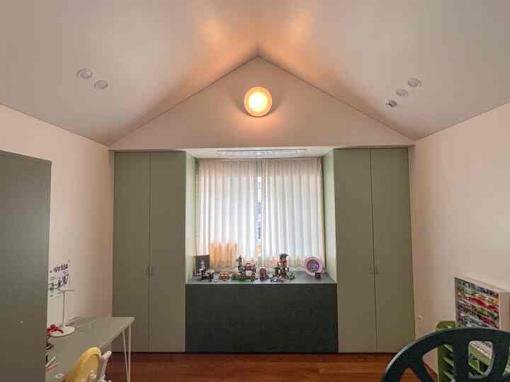 アイボリーとグリーンの色調の子供部屋、切妻屋根天井と窓辺の収納家具が配置された雰囲気のある空間