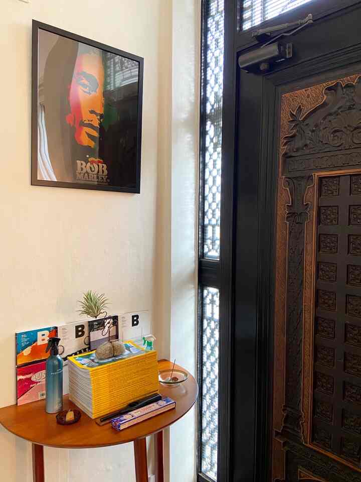 ナチュラルカラーの玄関、木製のナイトテーブルにポスターや雑誌、インセンスが配置された雰囲気のあるインテリア