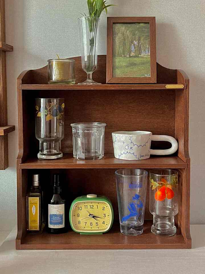 ダークな木目調の小さな収納棚にレトロなグラスや時計が配置されたミニマルな空間