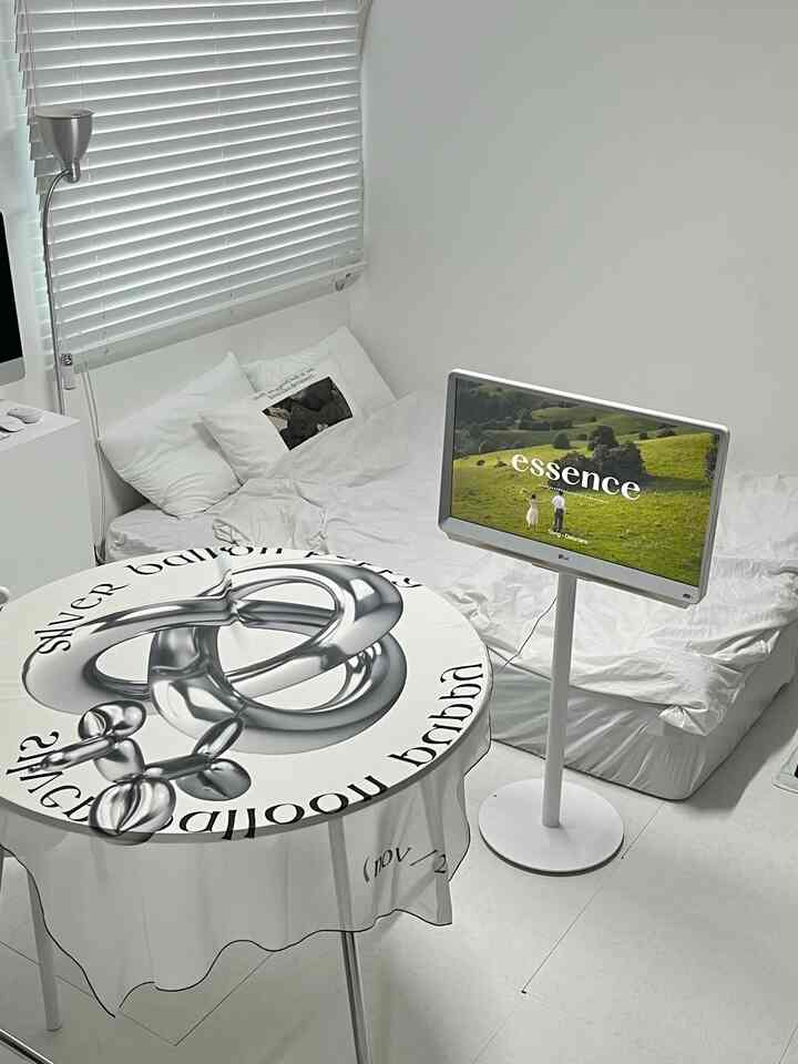 白を基調とした寝室で、ベッド、円形テーブル、テレビスタンドが配置されたすっきりとしたコンパクトな空間