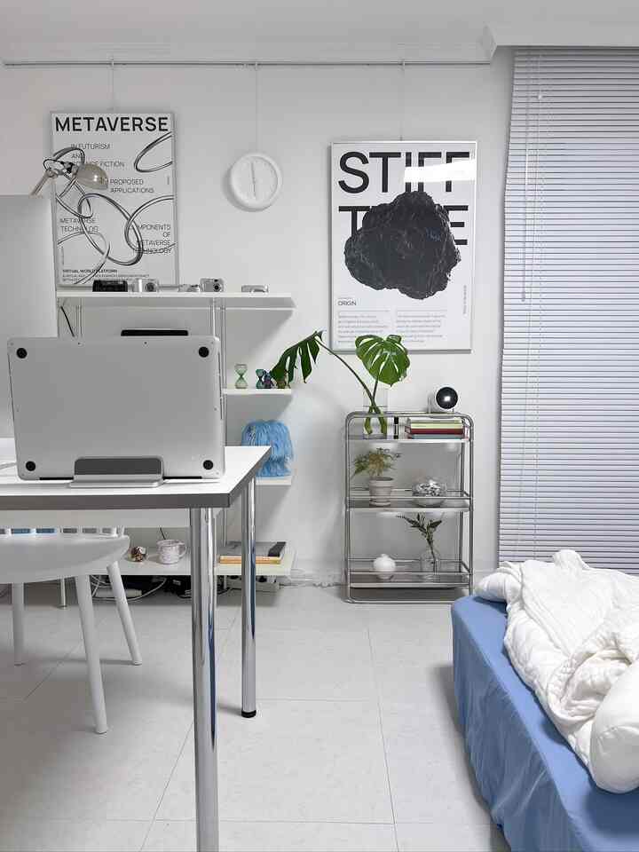 白と青のトーンで構成されたコンパクトな寝室兼ホームオフィス、棚とポスターが印象的に配置されたモダンなインテリア