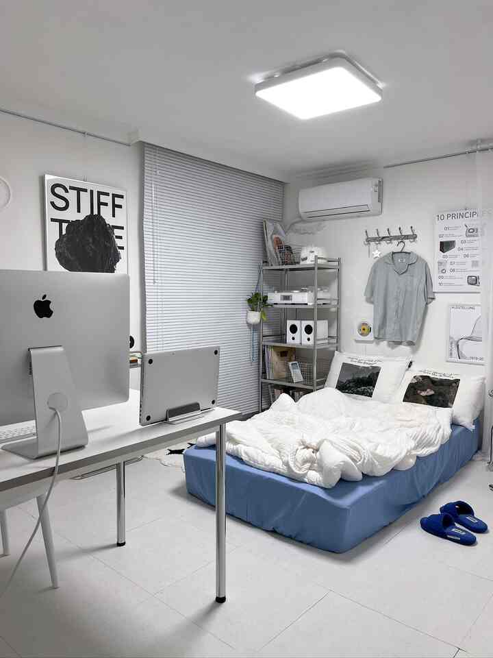 白と青のトーンが特徴的なモダンなワンルームの寝室、ベッド、デスク、棚、ブラインドが整然と配置された印象的な空間