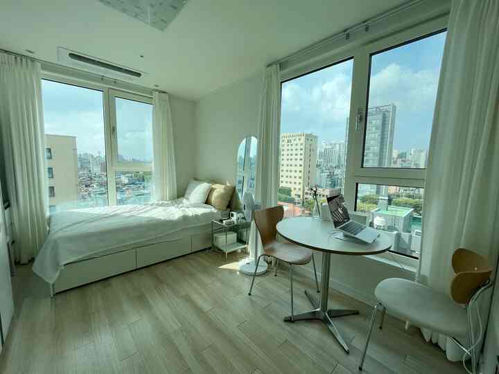 白とナチュラルトーンの寝室、一人用ベッドと小さな丸テーブル、ナイトテーブルと椅子が配置されたすっきりとした居心地の良い空間