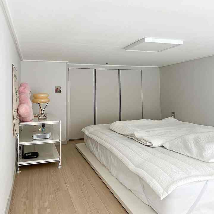 白と木目調が調和した低い天井の狭い寝室、ベッドとナイトテーブルが配置された居心地の良い空間