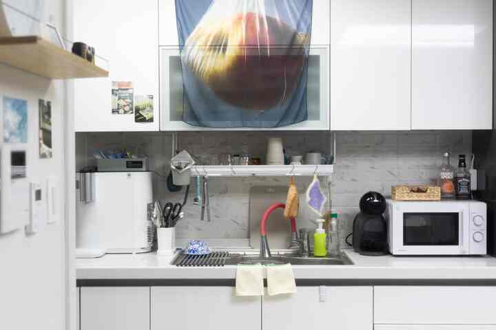 白とナチュラルトーンの縦長キッチン、シンクや電子レンジなどの調理器具が整然と配置された落ち着いた雰囲気のインテリア