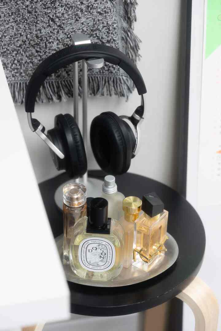 黒いスツールの上に銀色のトレイが置かれ、その上に複数の香水瓶とヘッドセットスタンドが配置された雰囲気のある空間
