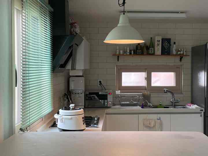 白とグリーンのブラインドが調和する清潔感あるキッチン、照明と電子レンジが配置された実用的なインテリア