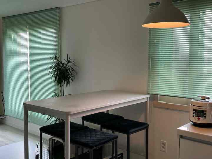 淡いグレーのダイニングテーブルと黒のカウンタースツールが配置された、薄緑色のブラインドのあるキッチンスペース