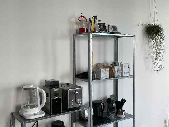 白い壁とシルバーのスチール棚が配置されたキッチンスペース、整理されたコーヒー用品のミニマルなホームカフェの雰囲気あるインテリア