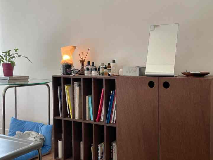 明るい壁とガラステーブルがあるナチュラルなブラウン調の収納キャビネットと本棚が配置されたすっきりとした室内空間