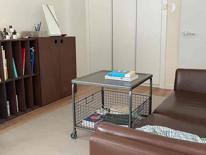 ブラウンのソファと金属製の収納付きサイドテーブルが配置された、白を基調とした居心地の良いリビング