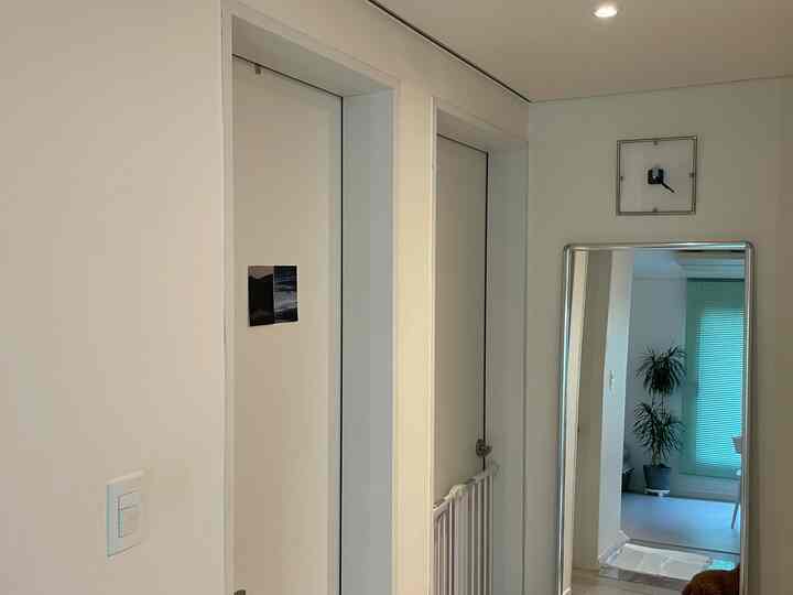 明るいナチュラルトーンの狭く縦長の廊下、全身鏡と壁掛け時計が配置された清潔感のあるインテリア