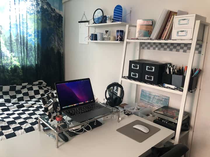 白と黒の配色が特徴的な寝室兼ホームオフィス、モニター台やデスク、棚が整頓された雰囲気のあるインテリア