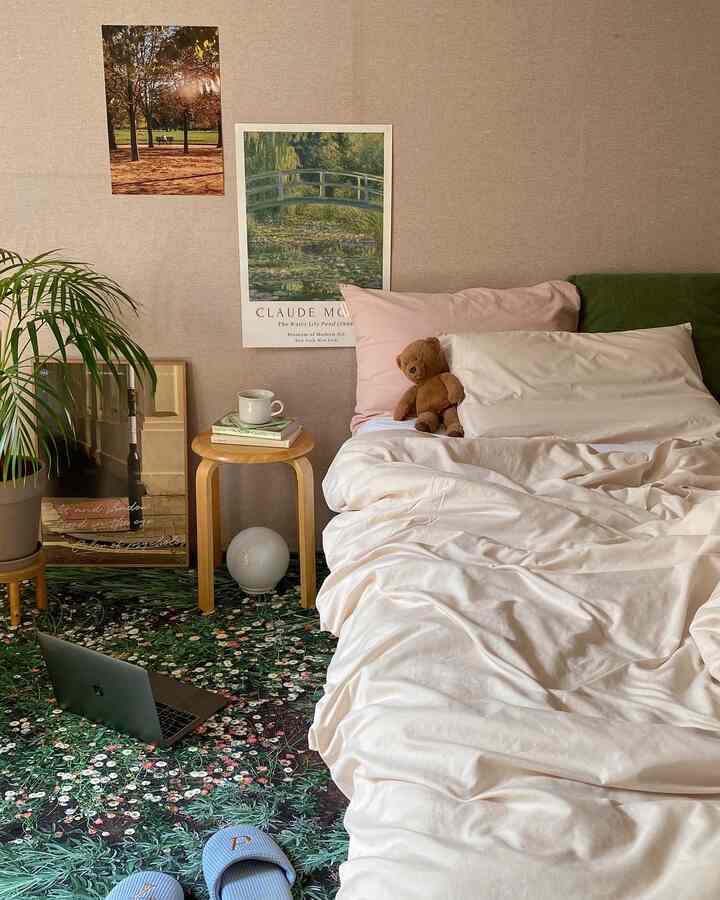 ベージュのトーンの寝室、枕と掛け布団があるベッド、花柄のラグ、スツール、植物が配置された落ち着いた空間