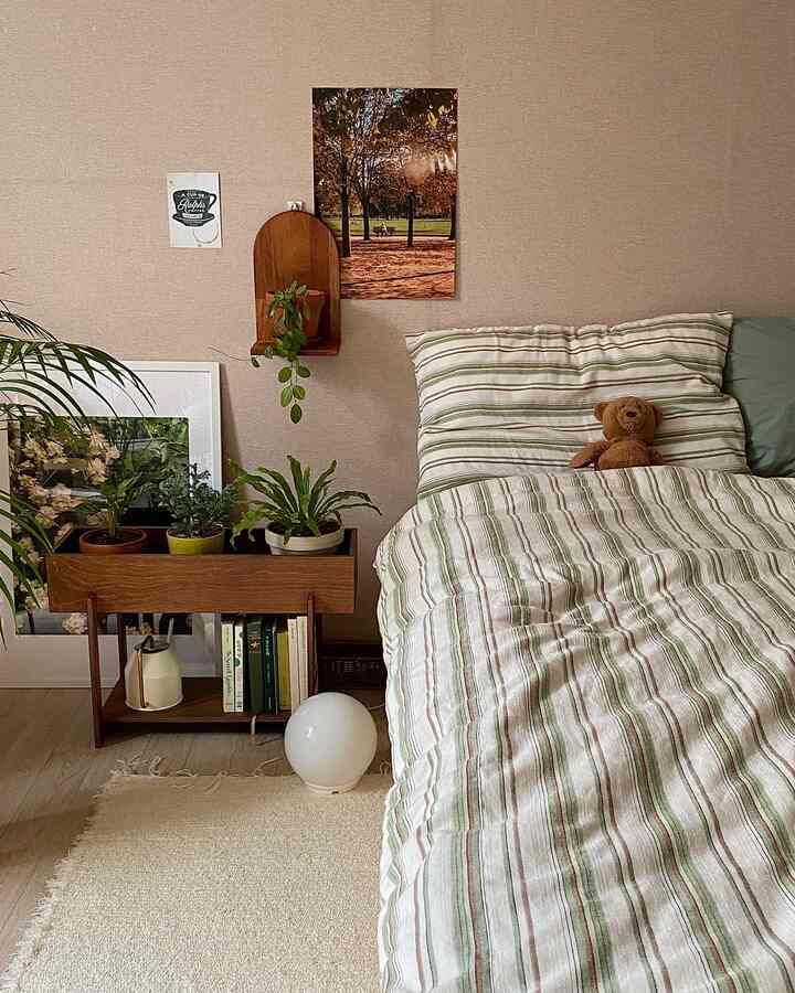 ベージュとグリーンのトーンの寝室、ストライプ柄の掛け布団カバーとプラントボックスが配置され、自然で温かみのある雰囲気のインテリア