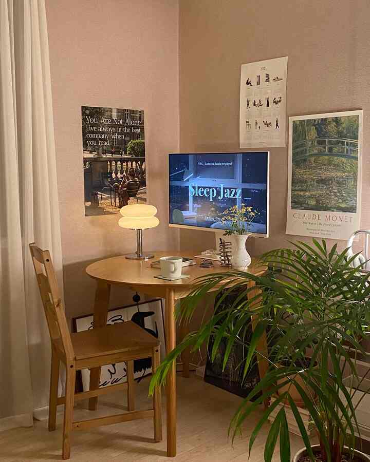 ベージュの壁とウッドトーンの円形テーブル、木製の椅子、テーブルランプ、ポスター、植物が配置されたナチュラルなおうちカフェの空間