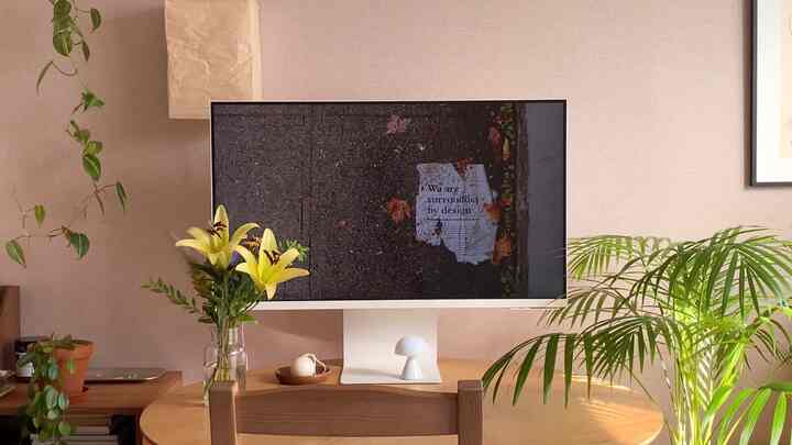 暖かいベージュのナチュラルなワンルーム空間、中央に丸テーブルがあり、その上に白いスマートモニターと緑の植物が調和した印象的なインテリア