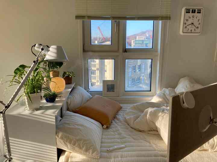 暖かな日差しが差し込む白を基調とした寝室、植物とスタンドライトが配置された自然な雰囲気のインテリア