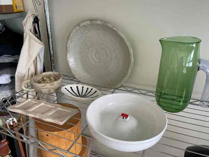 ナチュラルトーンのキッチン棚に多様な色の陶器のボウルと緑色のガラスピッチャーが置かれた雰囲気のあるインテリア