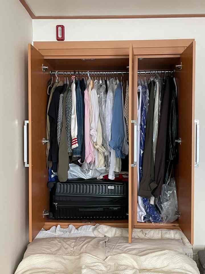 ベージュの木目調のビルトインクローゼットがある寝室、服とスーツケースが整理された収納空間