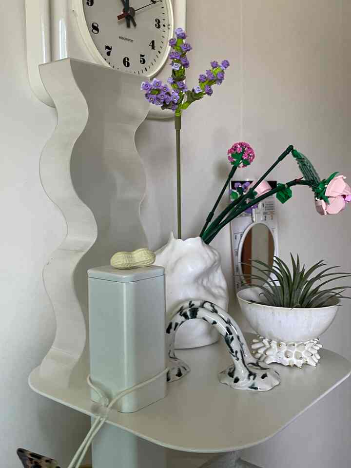 白とラベンダー色調のミニマルなインテリア、花瓶とレゴの花とオブジェが配置された落ち着いた空間