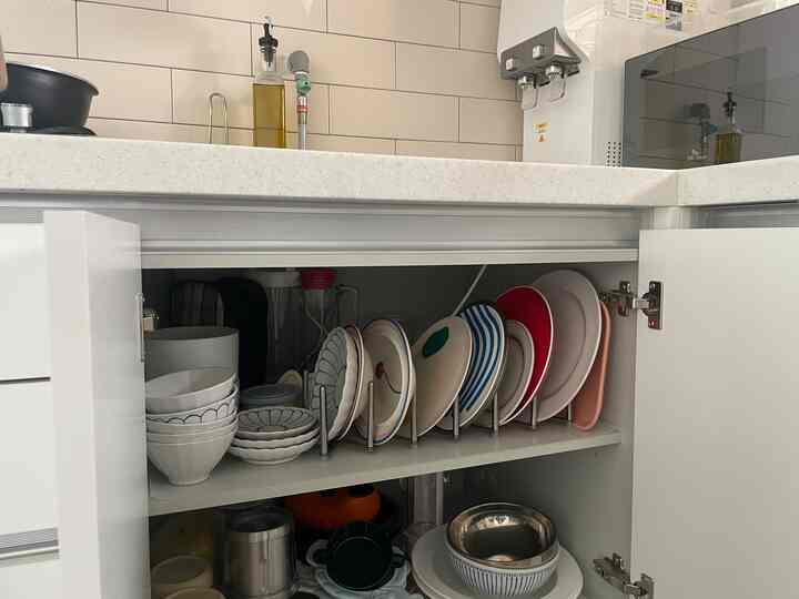 明るい白を基調としたキッチン、収納棚に整然と並べられた皿とボウル、カウンターには電子レンジが置かれている雰囲気のあるインテリア