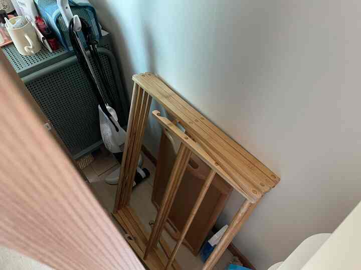 ナチュラルな色調のワンルームのコーナーに折りたたみ式木製物干し台と鏡の裏に隠された掃除機の収納スペース