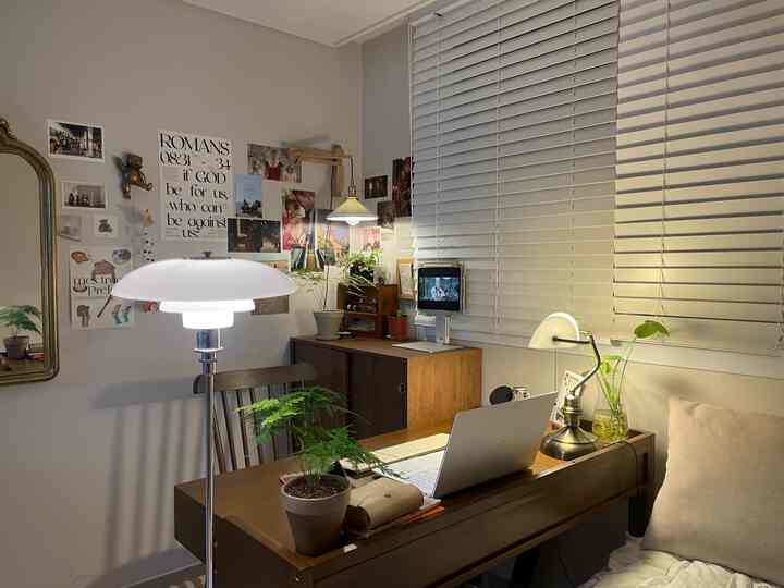 白いブラインドと木製のデスクが配置された落ち着いた一人用ホームオフィス、ポスターと植物が調和した自然なインテリア