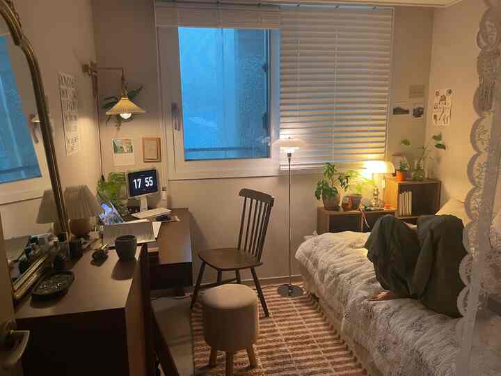 白と茶色のトーンでまとめられた小さな寝室兼ホームオフィス、木製家具と植物が配置された雰囲気のあるインテリア。