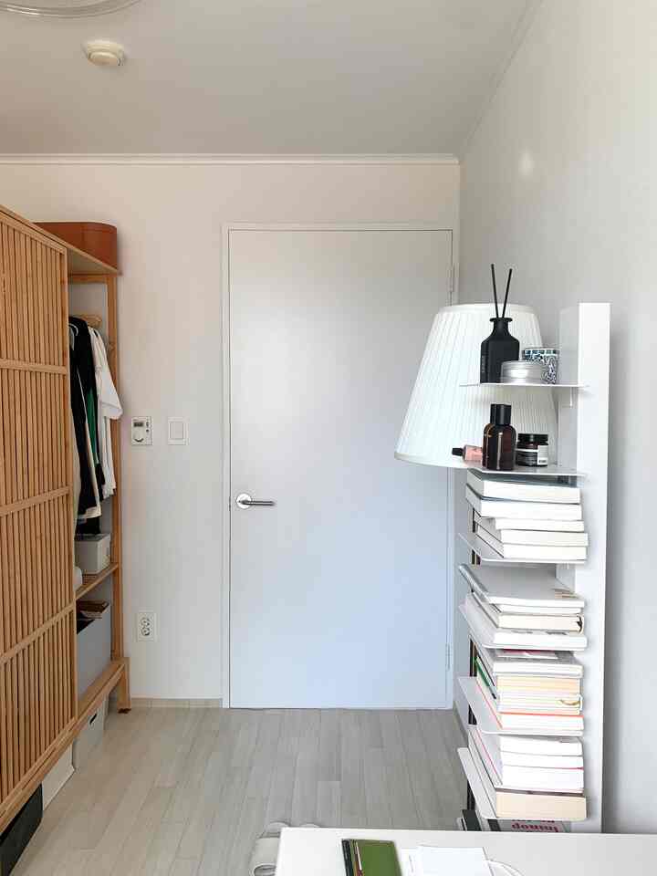 白い壁と木目調のクローゼットがあるシンプルでナチュラルな狭い部屋、本棚とフロアランプで温かみのあるインテリア