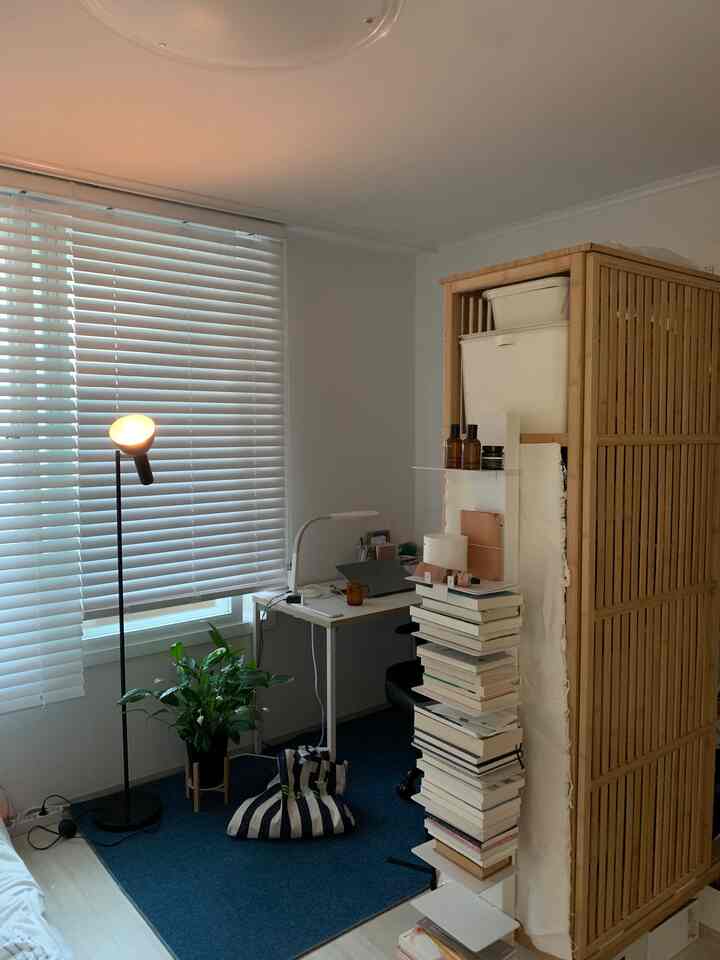 ホワイトとウッドトーンが調和する小さなホームオフィス空間、デスクと椅子、ブラインドの窓、観葉植物が配置された居心地の良い作業スペース