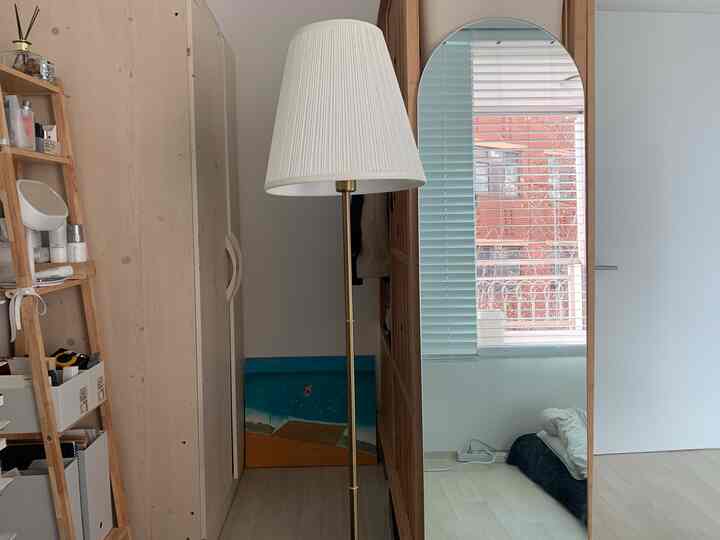 木目調と白を基調とした寝室空間、ワードローブと全身鏡、フロアランプが落ち着いたコンパクトな雰囲気を醸し出すインテリア。