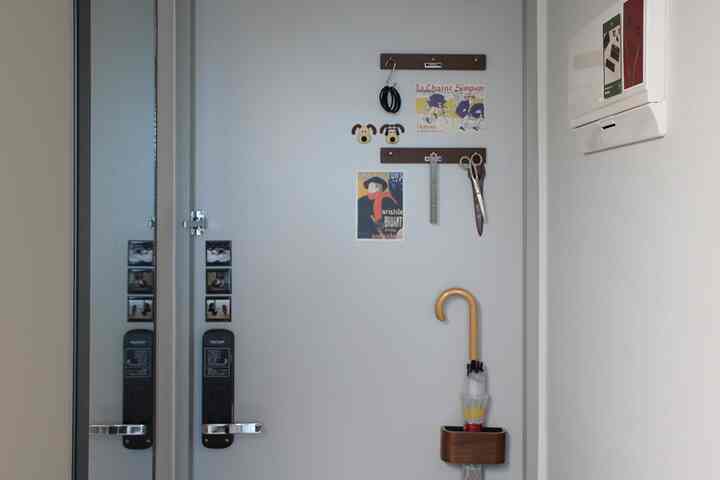 白い壁の玄関スペースに木目調のマグネット傘立てと複数のポスターが整然と配置されたモダンなエントランスインテリア